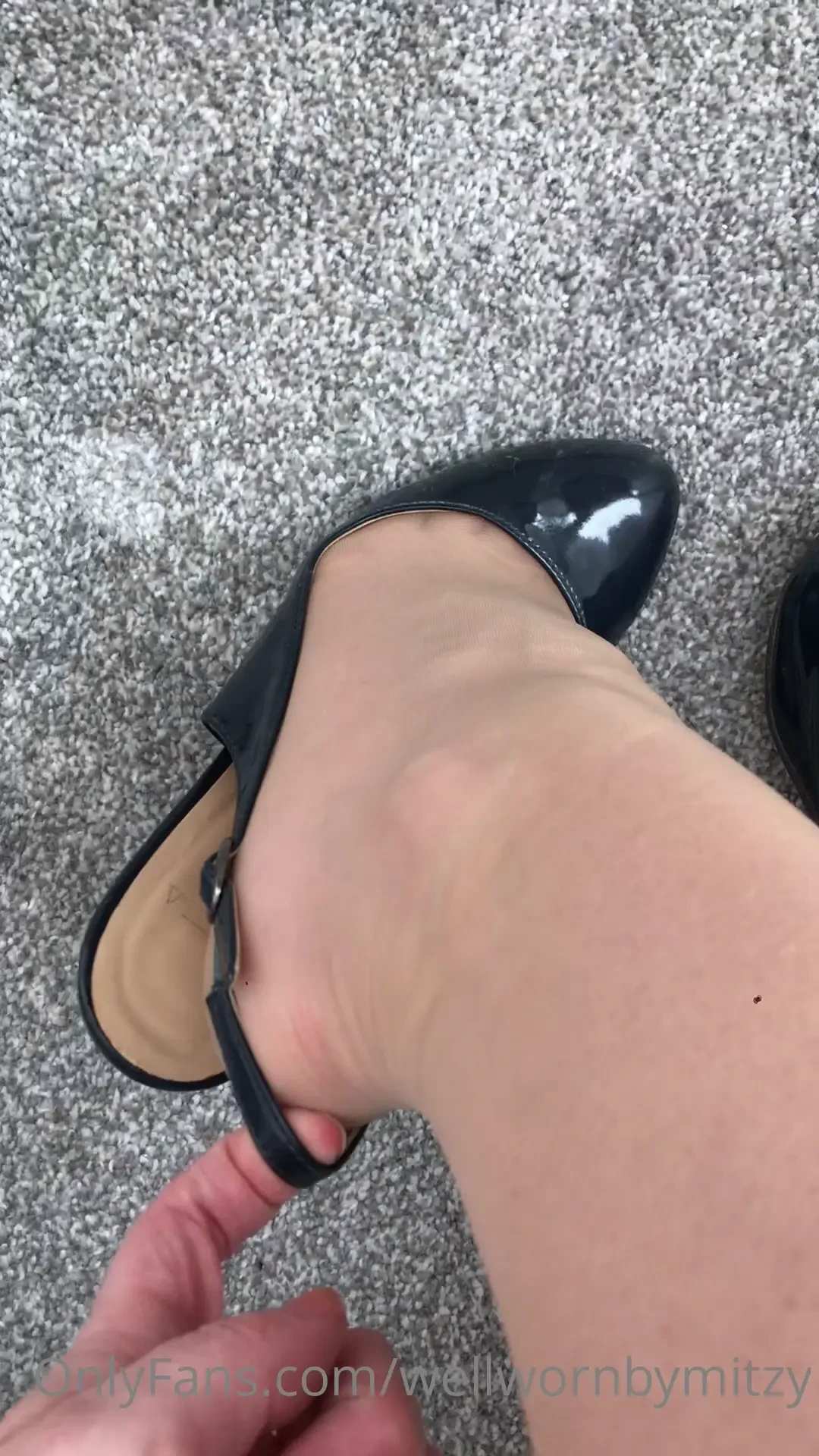 Putting on navy patent sling backs stretching the strap nude nylons 