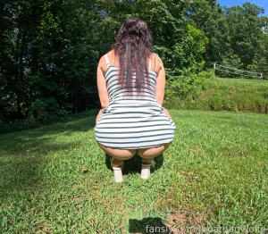 Squatting outdoors in sundress and heels near the park volleyball