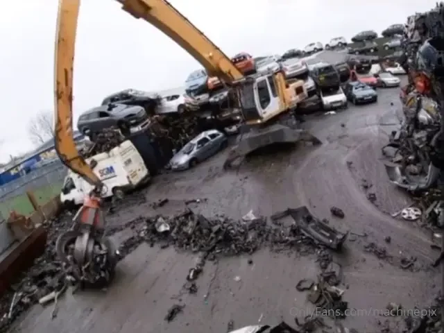 Claw excavator sweeping a salvage yard with a car 