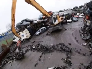 Claw excavator sweeping a salvage yard with a car